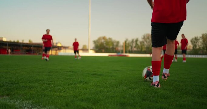 Low-angle view of youth soccer players in red uniforms practicing on a green grass field during warm evening team training