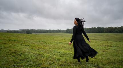 Obraz premium Smiling woman in flowing black dress running on green field.