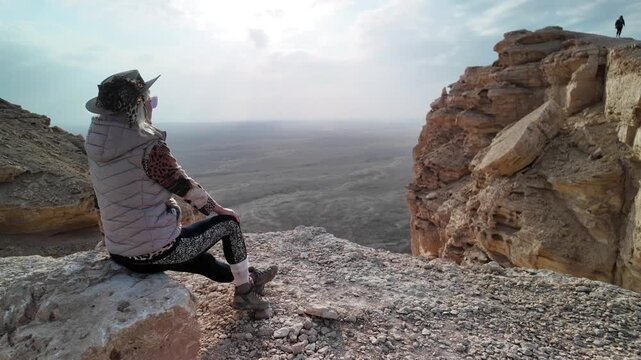 woman at sunset over the vast desert landscape viewed from the cliffs of the Tuwaiq mountain range in Riyadh, Saudi Arabia, showcasing the beauty and tranquility of nature