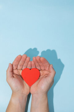 Male hands together holding a paper heart on a light blue background with copy space. Represents support, well being, empathy, and commitment to healthcare