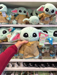 Naklejka premium Dubai, UAE - 24 may 2026: Grogu plush toy from Star Wars franchise held inside retail store with multiple character dolls on shelves, highlighting pop culture merchandise and fan shopping trend
