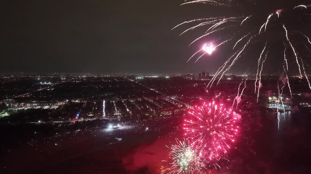 Circular aerial view orbiting vibrant Victoria Day fireworks exploding over Ashbridges Bay Park beach in Toronto, capturing bright pyrotechnic bursts over the illuminated night cityscape