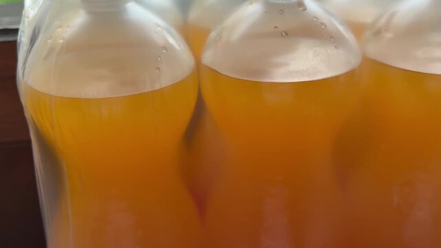 Big plastic bottles filled with orange beverage packed in transparent carrying bag for convenient transport during party, picnic and outdoor celebration.