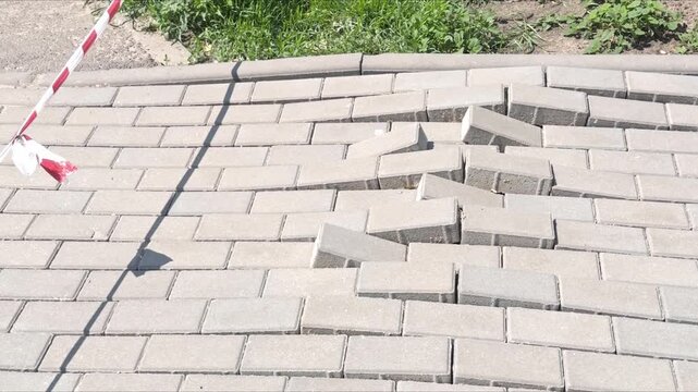 Damaged paving stones with displaced tiles and a hole, warning tape nearby