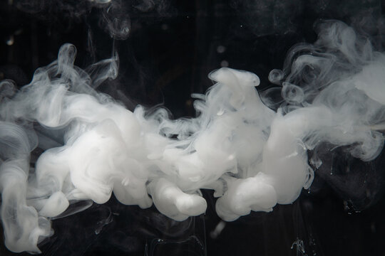 White smoke curls against a dark backdrop, forming unique shapes and patterns that slowly rise upwards