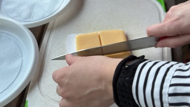 Close up of chef hands slicing yellow cheese on wooden board