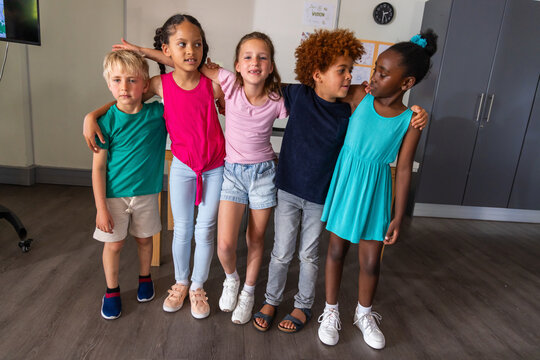 Diverse children standing shoulder to shoulder, linking arms in class, showing sneakers and clock
