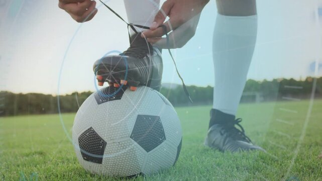 Soccer player placing cleat on ball, bending and tying laces on grass pitch, HUD guiding readiness