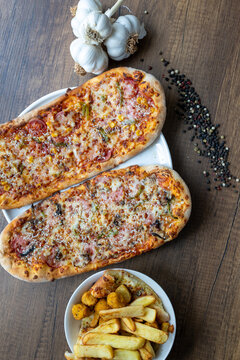 Close-up of sliced rectangular mixed pizza with rich toppings on wooden board