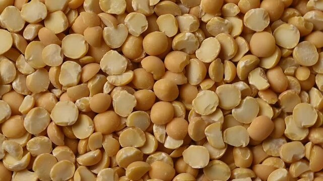 Close-up shot of dry organic split yellow peas pouring from a wooden bowl onto a heap against a beige background. Healthy vegan food ingredient. 
