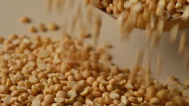 Close-up shot of dry organic split yellow peas pouring from a wooden bowl onto a heap against a beige background. Healthy vegan food ingredient. 

