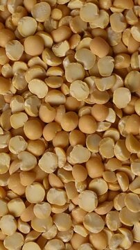 Close-up shot of dry organic split yellow peas pouring from a wooden bowl onto a heap against a beige background. Healthy vegan food ingredient. 
