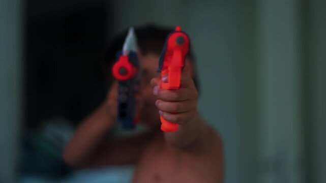 Young boy aiming colorful toy blasters toward camera during imaginative indoor play capturing childhood fantasy, excitement and playful pretend action at home