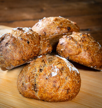 Four classic farm country bread buns stacked on a wooden chopping board. These homemade rustic rolls balls are made of organic wholemeal multigrain wheat flour for a sourdough recipe.