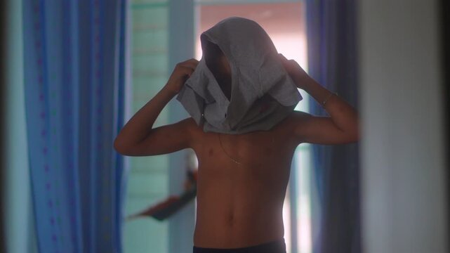 Boy pulling shirt over head during everyday dressing routine capturing childhood independence, self care learning and authentic family home lifestyle