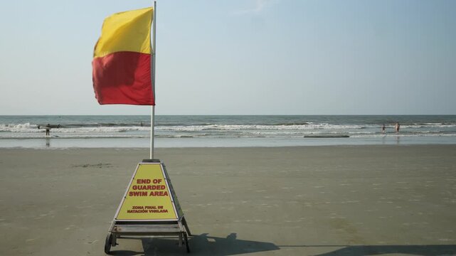 Lifeguard safety warning flag blowing in the wind at the beach while people enjoy their ocean vacation.