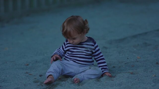 Little child sitting quietly in sandbox while touching sand during outdoor play capturing sensory discovery, calm reflection and authentic childhood exploration