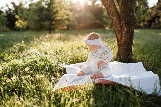 Cute baby girl sitting on blanket in sun light on green grass meadow outdoors. Summer season. Childhood.