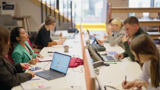 A diverse group of professionals are working at their desks in a contemporary office setting. Colleagues collaborate and focus on tasks, representing a productive business environment.