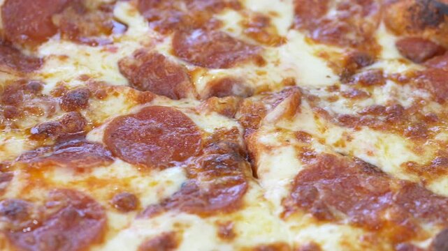 Macro closeup of pepperoni pizza reveals melted cheese texture and generous meat topping detail in appetizing food photography. Pizza detail footage suits food delivery app promotion, menu content