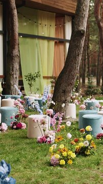 Vertical video. Empty wedding ceremony venue setup decorated before the event. Luxury floral arrangements, velvet poufs, and elegant textile curtains are captured in a pine forest background in 4K