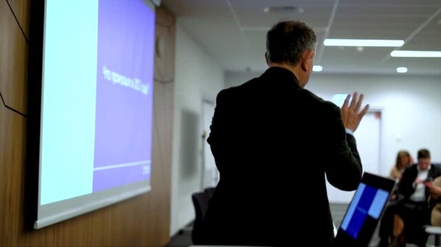 Lecturer speaking into microphone from behind during presentation, professional conference and public speaking event with projector background