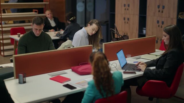 A group of diverse professionals are actively engaged in their tasks within a bustling open-plan office. Modern office employees focus on their computers and paperwork at individual workstations.