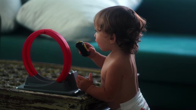 Toddler holding toy car beside loop racetrack during indoor play capturing imagination, motor skill development and authentic childhood exploration at home