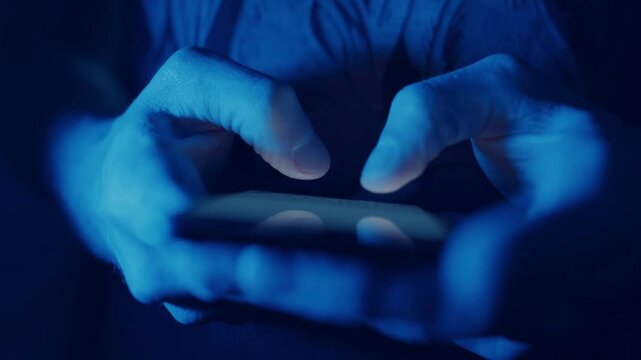 Close Up of Hands Typing on Smartphone Screen in Dark Room with Blue Light