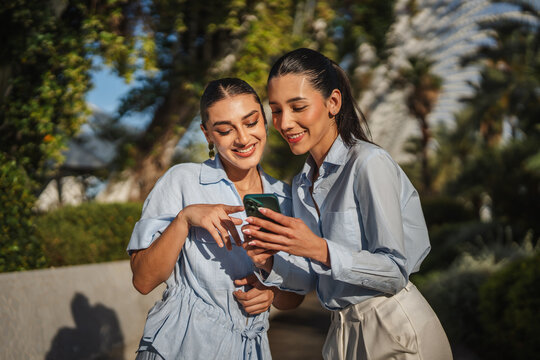 Two smiling women sharing content on smart phone