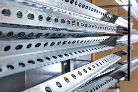 Close-up horizontal view of galvanized steel slotted strut channels and perforated metal support rails stacked horizontally on a display rack inside a hardware store or building supply warehouse, USA