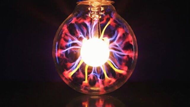 Macro shot of a clear glass light bulb containing swirling filaments of red and blue plasma energy radiating from a bright white central core isolated on a black background.