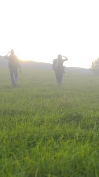 Hikers climbing hillside tailwind, Travelers traverse lush terrain with determined steps under bright sun