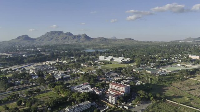 Drone flies north over city with Mudi Dam and mountains on the horizon on sunny afternoon in Blantyre, Malawi