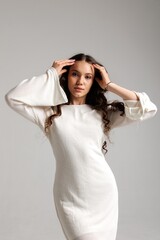 Fototapeta premium Model poses in a white dress with bell sleeves against a neutral background in a studio setting