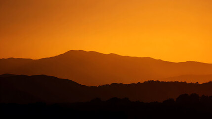 Obraz premium Dramatic mountain range silhouette at sunset: layer of distant hills under vibrant orange sky, showcasing natural landscape and warm evening light