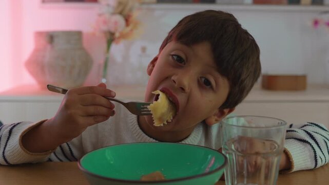 Boy eating ravioli pasta at dining table, childhood mealtime moment with homemade food and cozy family lifestyle concept