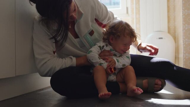 Mother caring for toddler during runny nose cleaning at home, authentic parenting moment with child resisting care and family support concept