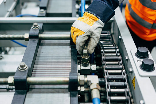 Worker in protective gloves adjusts industrial machinery with a chain drive system