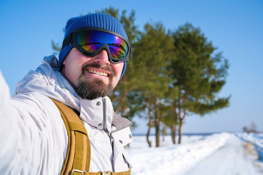 Smiling bearded man taking selfie near frozen reservoir during winter outdoor trip