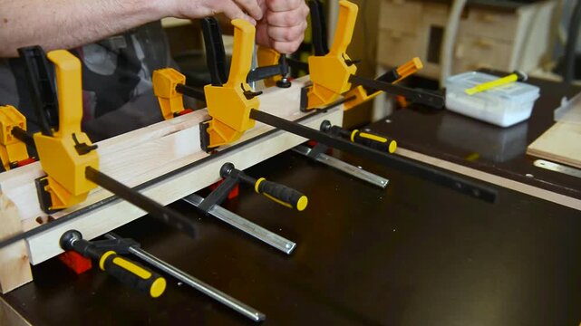 Skilled focused craftsman hands assembling clamps, securing bonding wooden boards. Precise woodworking, hands on expertise on mechanical setup, joinery artisan workspace, professional technique.