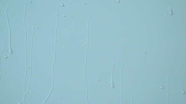 Drops and streams of water quickly flowing across a uniform background. A close-up of water flowing over a flat surface.