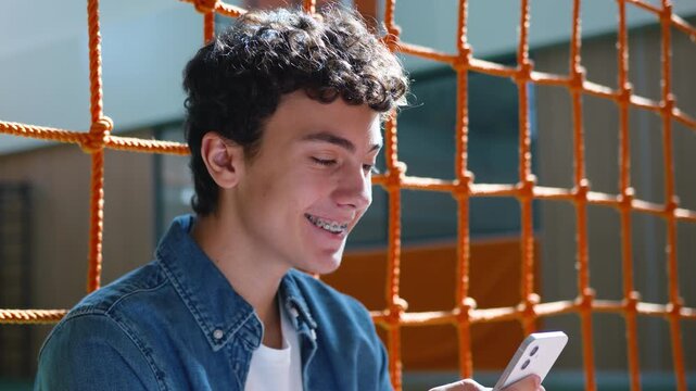 Caucasian boy amazed surprised teen Hispanic guy reading good news mobile phone at school male pupil Latina man teenager student looking at smartphone achieve excited wonder online university college