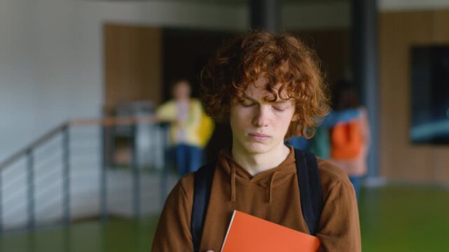 High school Caucasian sad lonely teen boy going frown couple teens push bullying upset frustrated man male guy teenager schoolboy students walking walk in university college corridor holding copybook