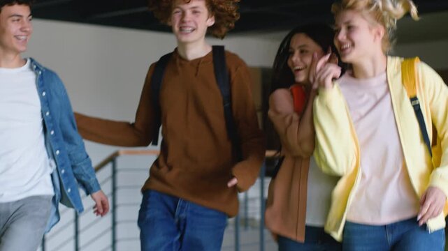 Happy teenagers guys girls students walk in school jumping celebrate end lessons four friends Caucasian males men boys women females pupils go corridor university college laugh smiling study achieve