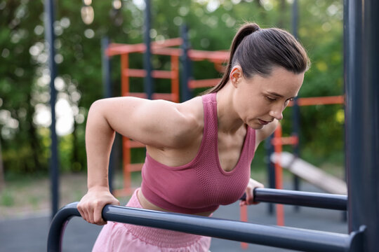 Athletic woman exercising on parallel bars at outdoor gym