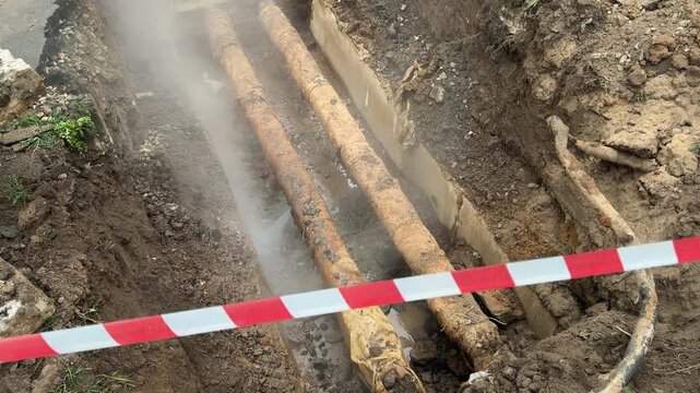 Old insulated heating mains releasing steam and water inside excavation site during underground utility restoration works