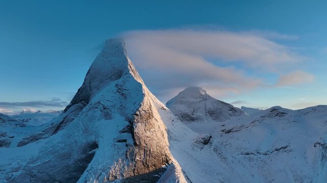 Aerial view of Stetind mountain peak covered in snow with wispy clouds at the summit under a clear blue sky in Narvik Municipality, Nordland, Norway.