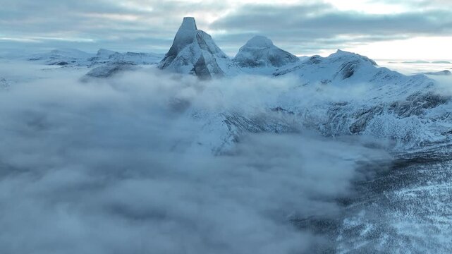 Aerial view of Stetind mountain peak rising above a thick layer of clouds and snow-covered slopes in Narvik Municipality, Nordland, Norway.