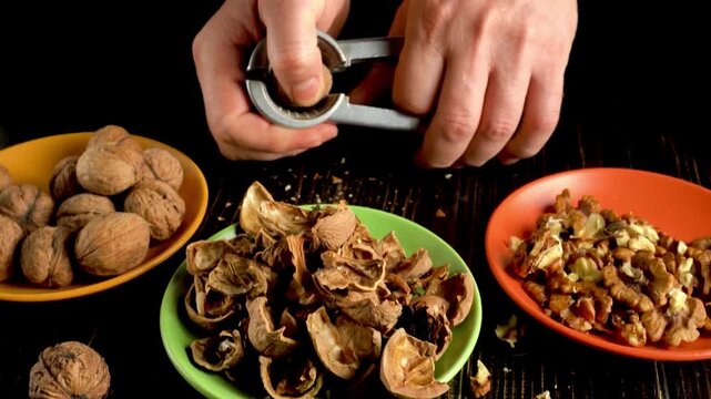 Hands cracking open walnuts using a nutcracker, with shells and nuts arranged on colorful plates in a well-lit kitchen setting